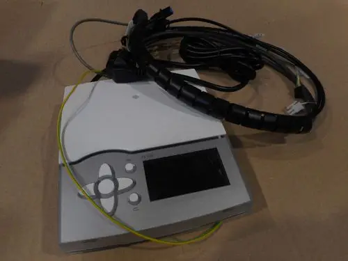 Gerät von Remeha mit Display und Steuerungsknöpfen, umgeben von Elektroanschlüssen und Kabeln. Auf einer neutralen Unterlage platziert.